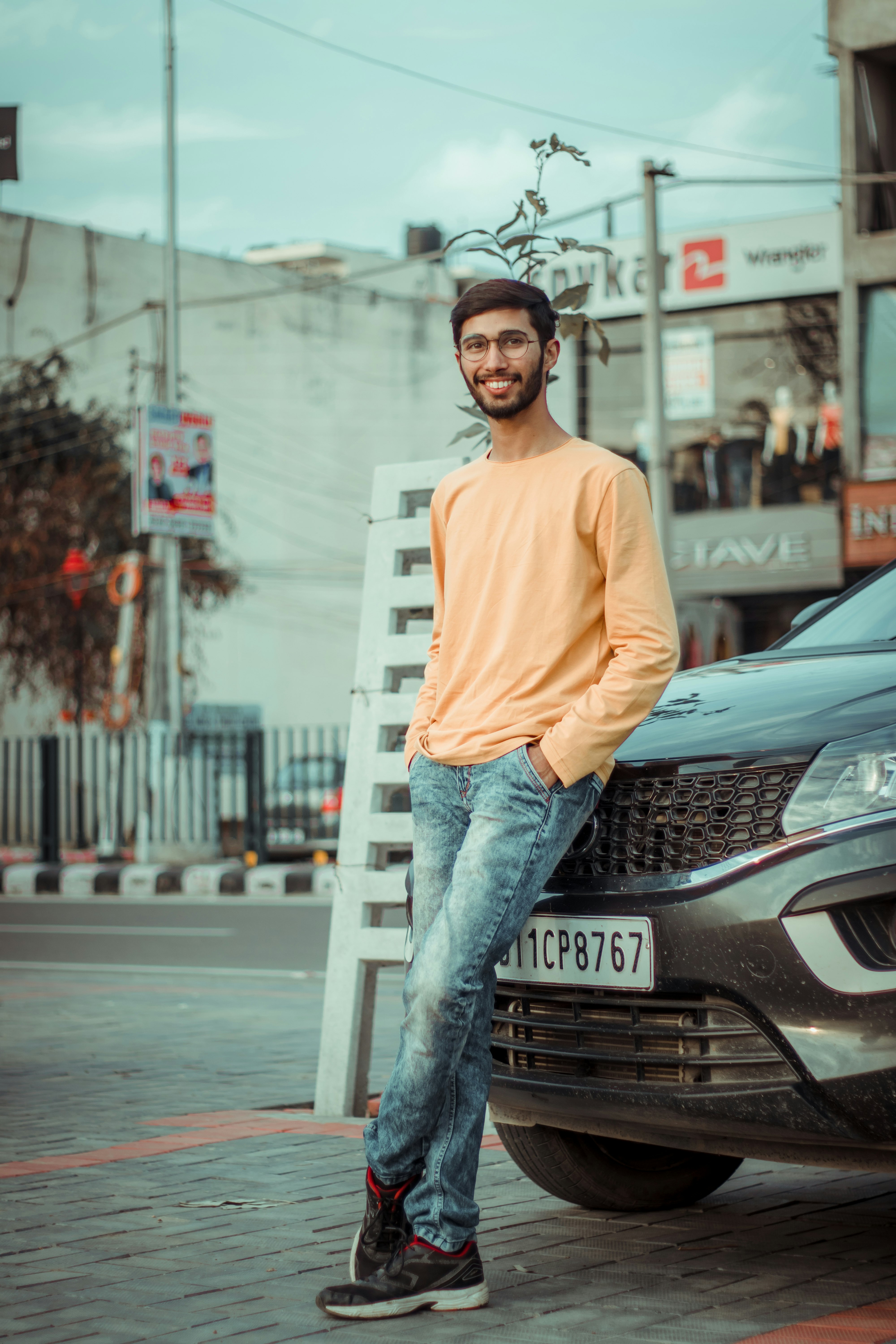 man in brown long sleeve shirt and blue denim jeans leaning on black mercedes benz car